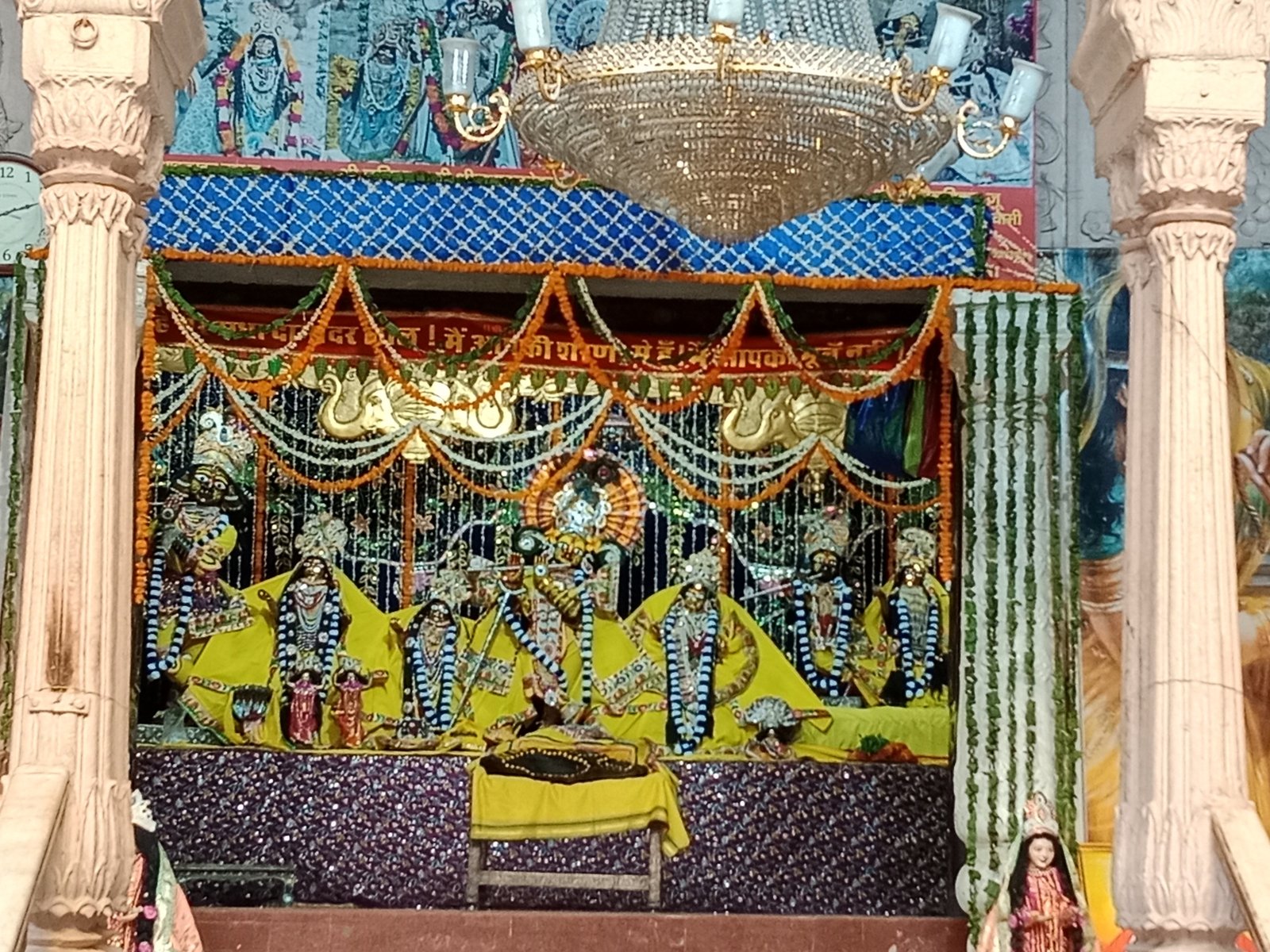 The garlanded deities of Radha Damodar on their altar, seen through the temple's carved stone columns